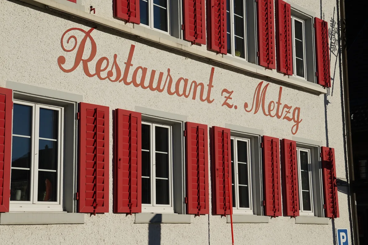 Das Restaurant zur Metzg in Russikon. Eine helle Fassade mit roten Fensterläden.